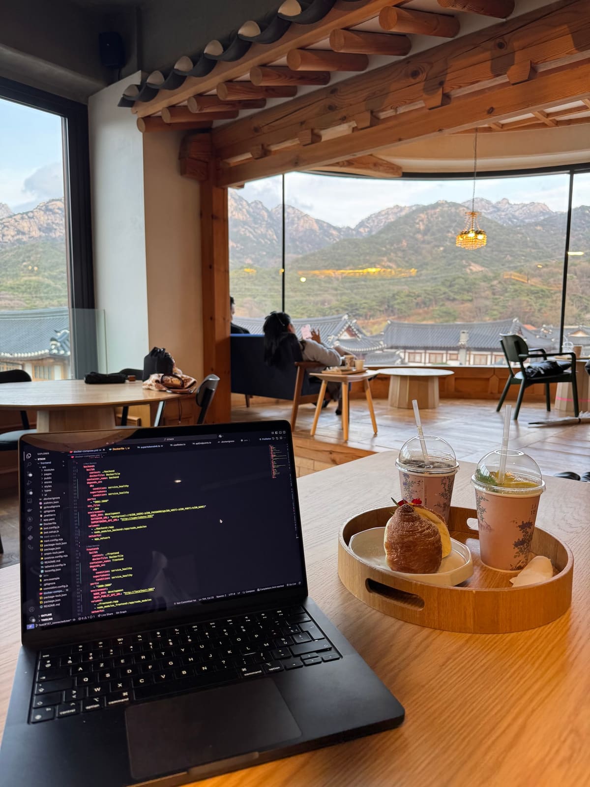 An open laptop showing code, in a café with traditional wooden beams, facing the mountains