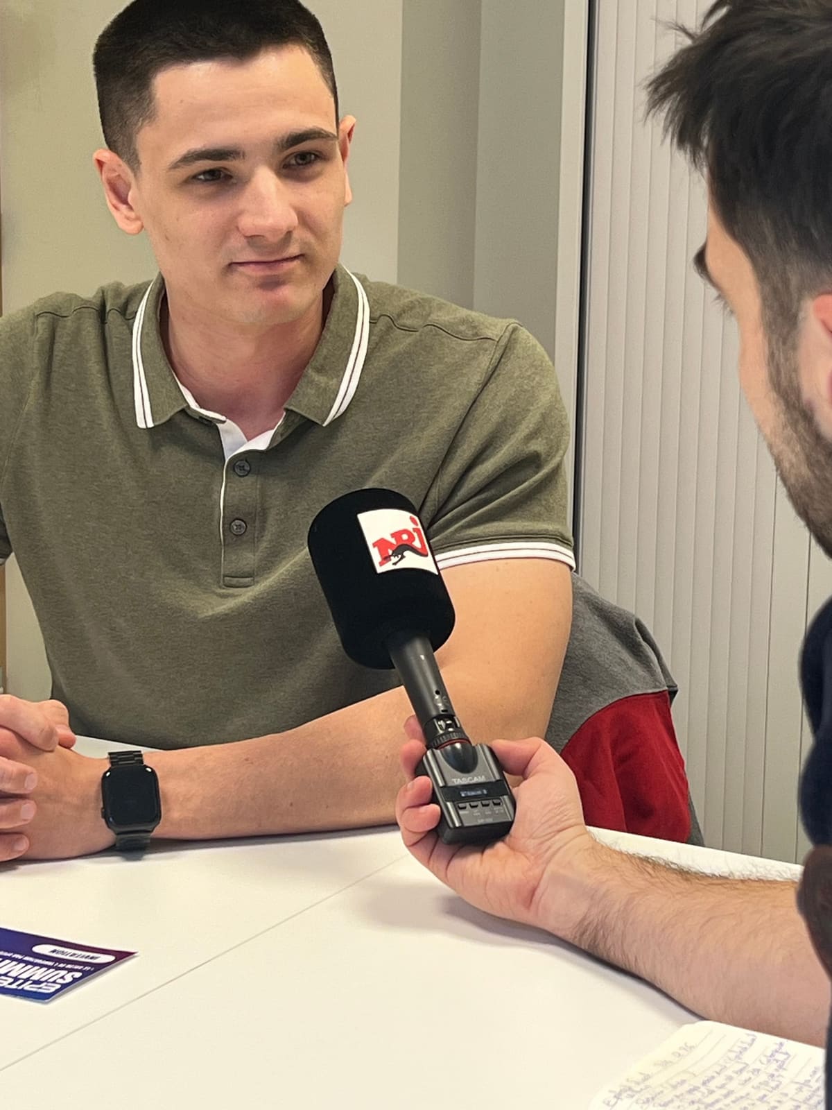 William Stoops listens to a question, facing the NRJ microphone a journalist holds out